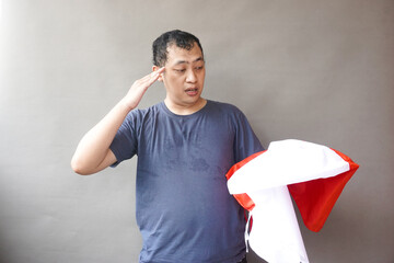 Happy Indonesian man using blue shirt feel proud nationalism when holding flag on his hand celebrate Indonesia Independence Day on grey background