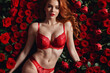 © SOLOTU - Sexy woman with red hair in red lingerie bra lying on carpet from red rose's buds and petals