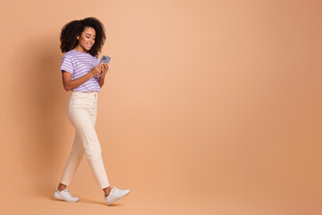 Wall Mural - Full body portrait of pretty young girl use phone walk empty space wear t-shirt isolated on beige color background