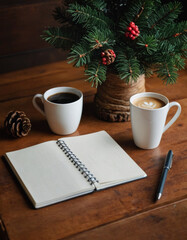 New year resolutions background. Wooden table with blank notebook page, pen, coffee cup and decorated fir tree branch. Goals, resolutions, plan, action, checklist, shopping list concept