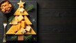 © Indi - creative arrangement of cheese slices and crackers on dark plate in shape of Christmas tree, wooden surface, banner with copy space. marketing for gourmet cheese brands specialty food stores concept.