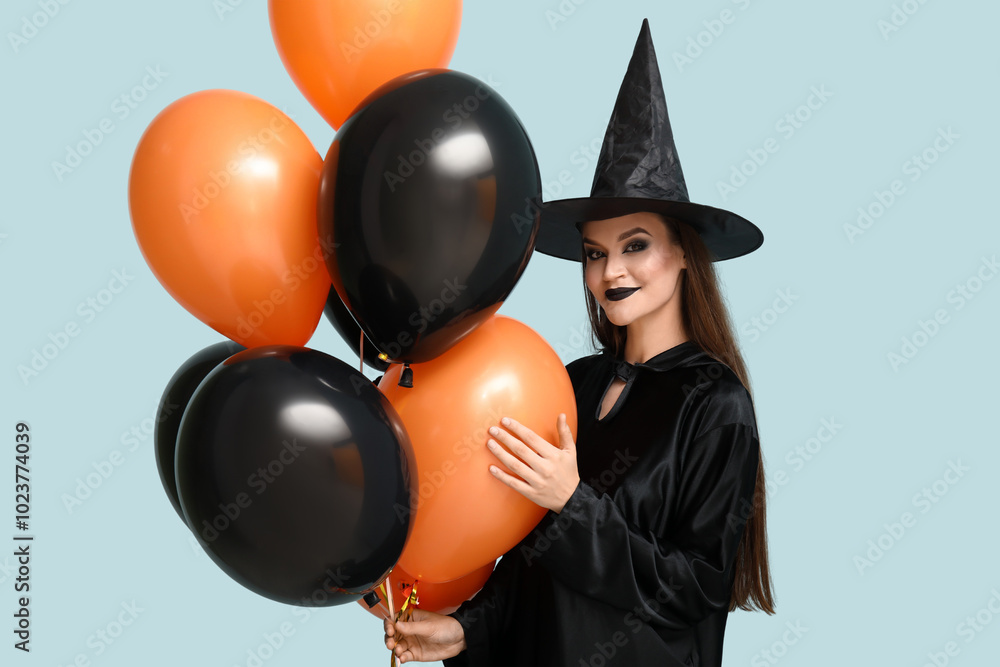 Young woman dressed for Halloween as witch with balloons on blue background