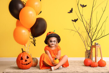 Wall Mural - Little girl dressed for Halloween with pumpkins and balloons near yellow wall