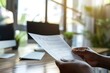 © Yuliia - close-up shot of a person's hand holding a curriculum vitae with an office desk and computer in the background.