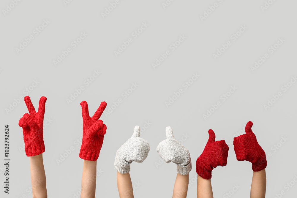 Hands in warm gloves showing victory gestures and thumbs-up on grey background