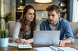 © Yuliia - young couple sitting together at their laptop, discussing family finances and calculating their income and expenses.