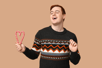 Wall Mural - Handsome young man in warm sweater with candy canes on beige background