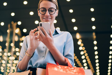 Wall Mural - happy millennial female shopaholic continue shopping online via smartphone gadget after time in mall
