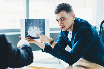 Serious male partners discussing new finance graphic with corporate productivity for future startup project, concentrated men communicating in office company and analyzing exchange occupation