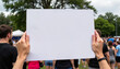 © Iuliia - Hands holding a blank sign at a public gathering with a crowd in the background, copy space