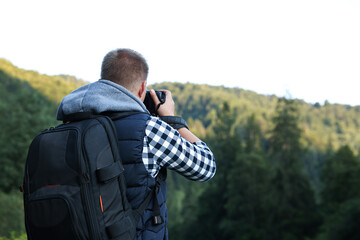 Wall Mural - Photographer with backpack and camera taking picture of beautiful mountains, back view. Space for text