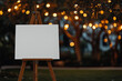 © Vitalii - A white blank template canvas on a wooden easel in a green park in the background at night