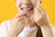 © New Africa - Girl with braces cleaning teeth with dental floss on orange background, closeup