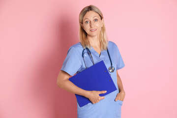 Canvas Print - Portrait of doctor in medical uniform with stethoscope and clipboard on pink background