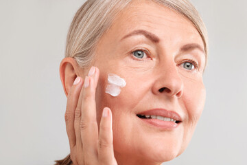 Canvas Print - Senior woman applying face cream on light background, closeup