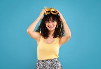 Wall Mural - Happy young woman with carnival mask on light blue background