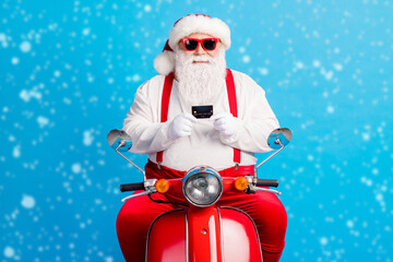 Wall Mural - Photo of grandfather grey beard ride retro scooter hold demonstrate debit card wear santa claus x-mas costume suspenders sunglass white shirt cap gloves isolated blue color background