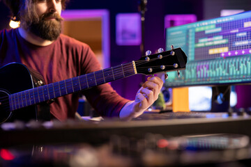Leinwandbilder - Musical artist tuning his acoustic guitar by twisting the knobs, preparing to play cool instrument in home studio. Musician songwriter recording tunes to create new song, mixing mastering gear.
