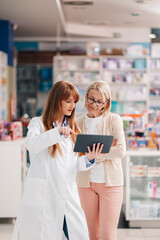 friendly pharmacist showing information on digital tablet to customer in drugstore