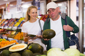 Family in the grocery section of supermarket, father and his teenage daughter buying melon