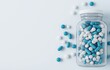 © pisan thailand - Assortment of different colored pharmaceutical pills capsules and tablets in a clear glass jar or container on a clean minimalist light colored background  Concept of medicine healthcare drug therapy