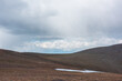 © Daniil - Ascetic landscape with high stony mountain pass with snow and stone hills under rainy low cloud in dramatic sky. Scenic view to alpine valley with snowfield in rain time in cloudy changeable weather.