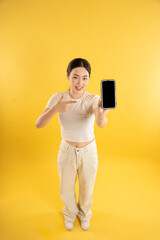 Wall Mural - Full body image of young Asian girl using phone and posing on yellow background