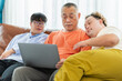 © JU.STOCKER - Grandfather and grandson using laptop doing a video call in living room, Senior asian man having a good time sitting on couch at home with adult son