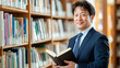 © Nattapol - confident man in suit stands in library, holding book and smiling warmly. shelves are filled with various books, creating inviting atmosphere for reading and learning