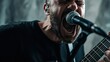 © Johannes - Portrait of rock singer man keeping electric guitar and static acoustic mic, sings a song loudly on grey background. Concept of rock music and rave