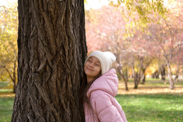 Girl enjoying warmth of sunlight on beautiful autumn day outdoors in park and breathing in fresh air with closed eyes. Quiet life and simple pleasures. Nature, balance and joyful rest.