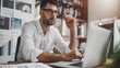 © NMS Images - Focused businessman at desk with financial documents and laptop displaying earnings reports, conveying determination and attention to financial data analysis.