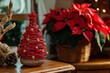 © michnik101 - Creative christmas tree homemade from stiff starched red string with small golden baubles and red star. Wicker stand and wooden table, Blurry red poinsettia flowers at the background.