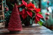 © michnik101 - Original christmas tree homemade from stiff starched red string that creates cone shape. Wooden stand and table, Blurry red poinsettia flowers at the background.