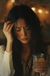 © Elena - A woman with glass of whiskey, sits with her eyes closed, holding her head with one hand. Thinking about problem at work or relationship problems, feeling desperate and depressed, alcohol addiction