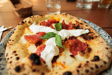 dettagli di una pizza in primo piano, fatta con la ricetta classica, farcita con salsa di pomodoro, mozzarella, fette di salame piccante, foglie di basilico e burrata