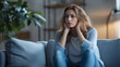 © keystoker - A woman with long hair sits on a couch, looking pensive and worried while holding her head in her hands, reflecting on her emotional state, copy space