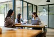 © YiuCheung - Three women sit around a wooden table in an office setting.