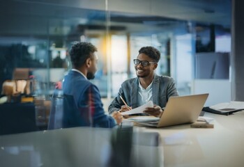 Two men in business attire are having a conversation in an office setting.