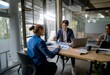 © YiuCheung - Three coworkers collaborate around a wooden table, reviewing documents and using a laptop.