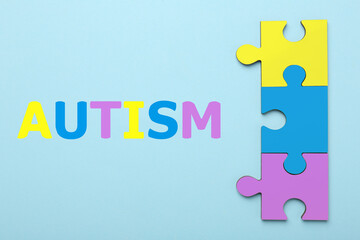 Wall Mural - Autism word and colorful puzzle pieces on light blue background, top view