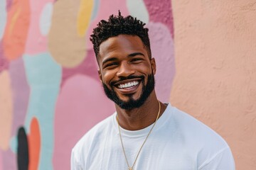 A smiling black man in a white t-shirt stands in front of a colorful wall.