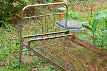  part of one painted old iron heavy blue industrial  antique dirty rusty broken empty retro bed  stands on the green grass near the leaves during the day on the street