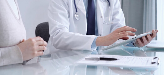 Doctor consultation with patient in modern clinic. Healthcare professional discusses medical information with a woman, holding a tablet computer. Medicine