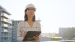 © volha_r - Woman construction engineer wearing white checked blouse and hard hat is making notes on a clipboard while inspecting a building site at sunset, front view. Architecture and engineering concepts