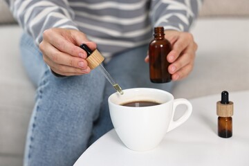 Canvas Print - Young woman putting CBD tincture into cup with drink at white table, closeup