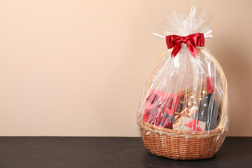 Canvas Print - Wicker gift basket with wine on black textured table against beige background, space for text