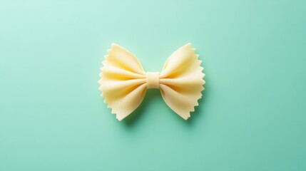 A single farfalle pasta bow isolated on a soft pastel mint green background, centered with subtle shadow.