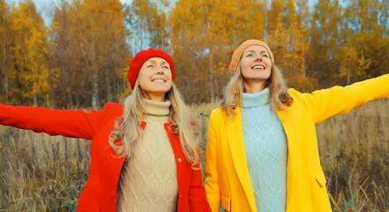 Wall Mural - Happy two women friends in autumn park enjoying warm weather, stylish girlfriends smiling together