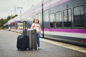 girl on a railway station. Little child waiting for a train on a platform. Kid with a luggage ready to travel.